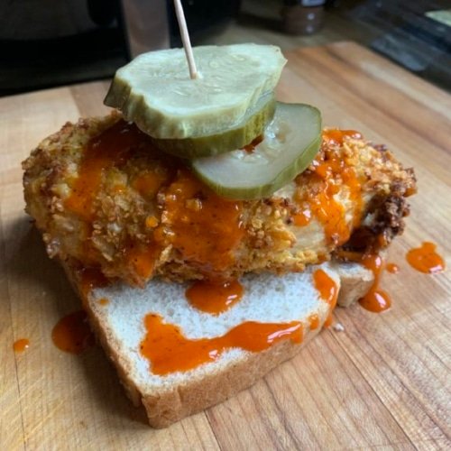 this shows a picture of a breaded and air fried chicken breast with hot sauce and pickles