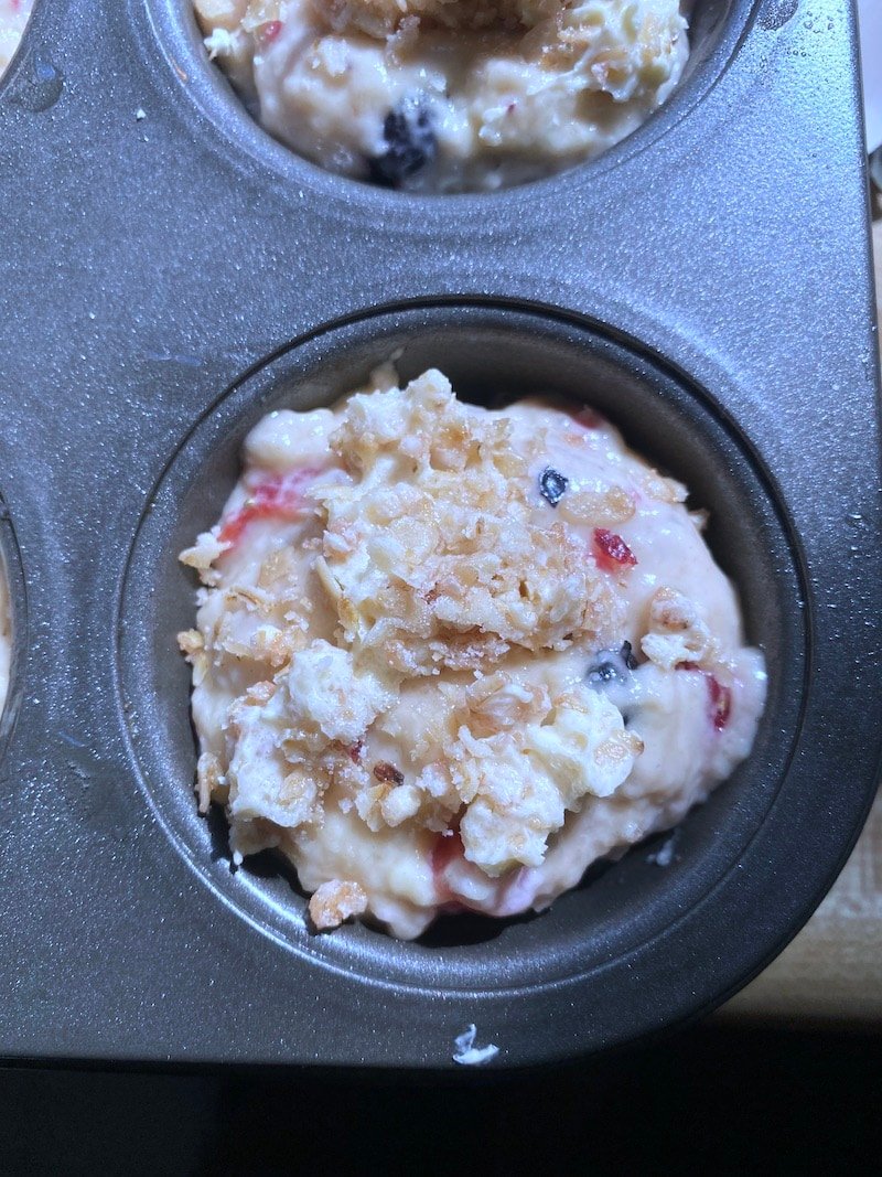 This photo shows muffin batter in a muffin tin with a granola butter topping