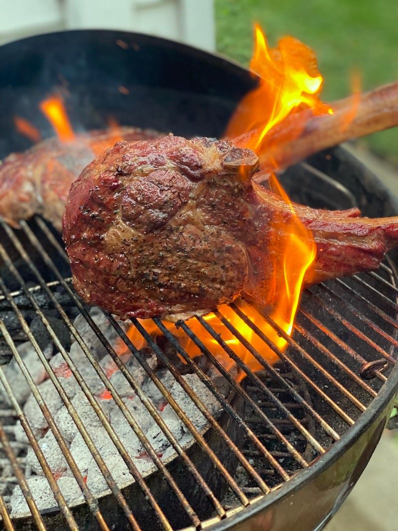 this shows a tomahawk steak being grilled over high open flames on a grill