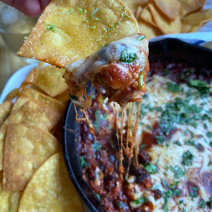this is a photo of a chip being dipped into black bean dip with cheese