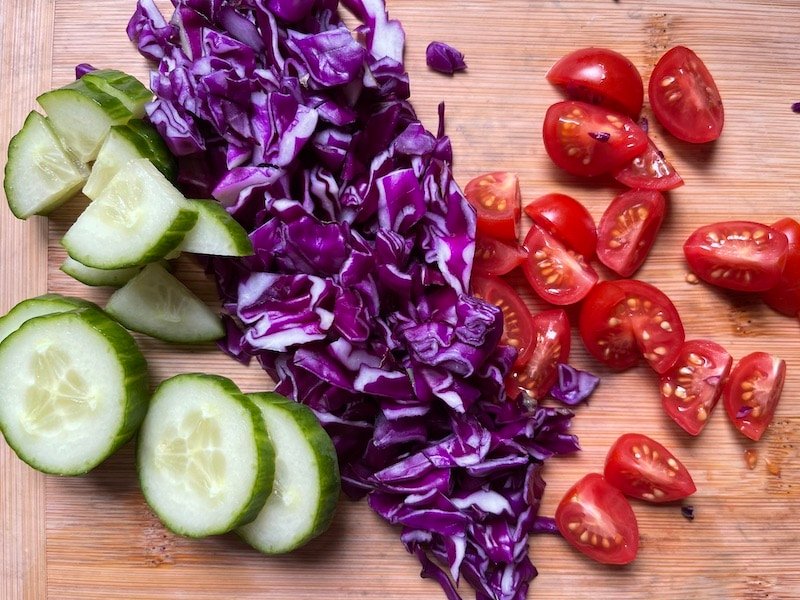 this is a photo of cut cucumbers, red cabbage and cherry tomatoes