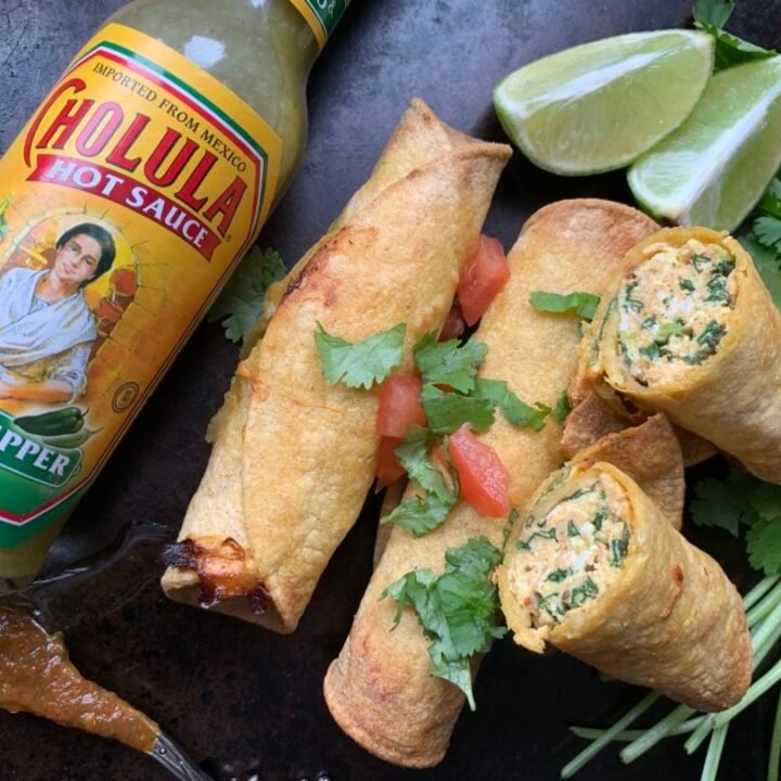 This is a plate of breakfast taquitos with hot sauce.