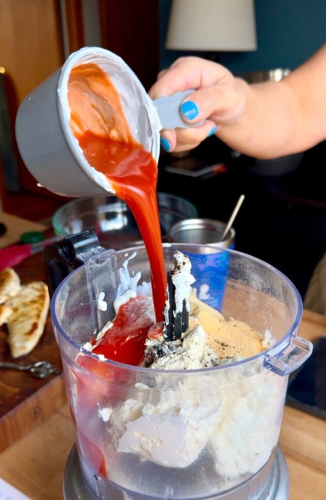 buffalo sauce being added to ingredients to make buffalo chicken dip